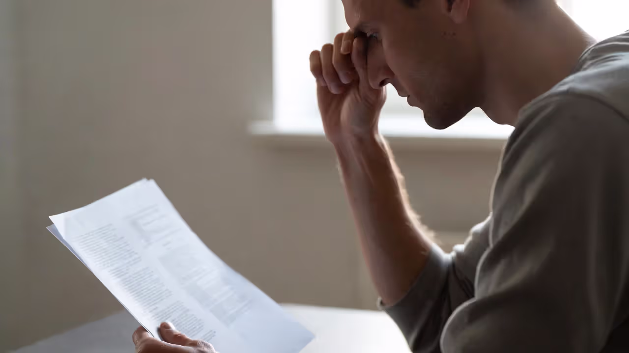 Person sitting at a table looking stressed while reviewing a paper with two columns