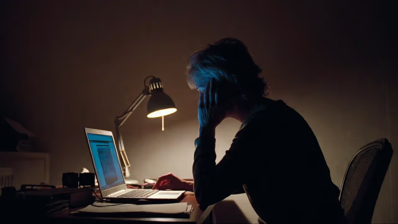 Tired professional sitting at desk at night with laptop and documents